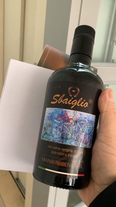 Flasche mit schwarzer Etikette, bunte Grafik und weißem Karton im Hintergrund.
