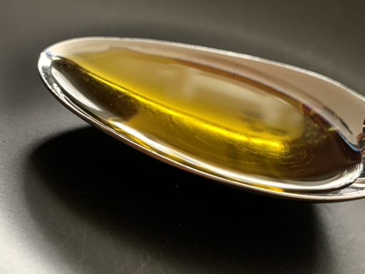 Löffel mit goldgelbem Öl auf schwarzem Hintergrund.